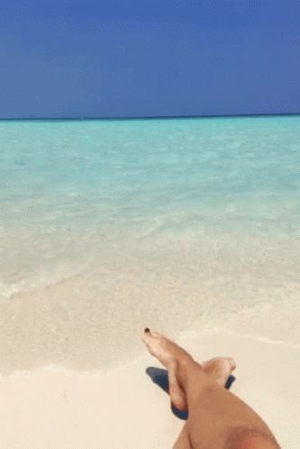 a person is laying on a beach with their feet crossed