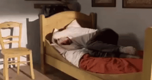 A Person Is Laying On A Bed In A Room With A Yellow Chair . GIF