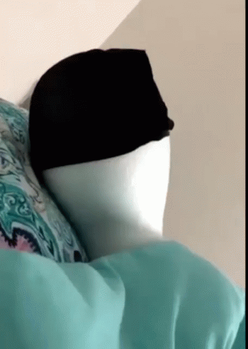 A Person Is Laying On A Bed With A Hat On Their Head GIF