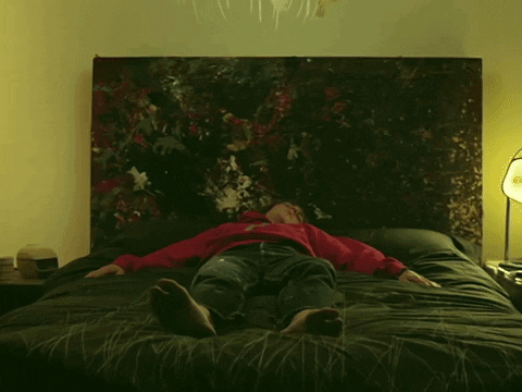 A Person Is Laying On A Bed With A Painting Behind Them GIF
