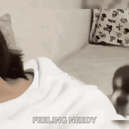 A Person Is Laying On A Bed With The Words `` Feeling Needy '' Written On The Bottom Of Their Shirt . GIF