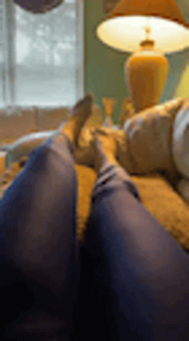 a person is laying on a couch with their feet up in front of a lamp .