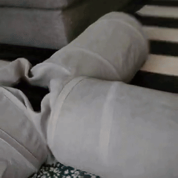A Person Is Laying On A Couch With Their Legs Crossed And A White Pillow On Top Of Them . GIF