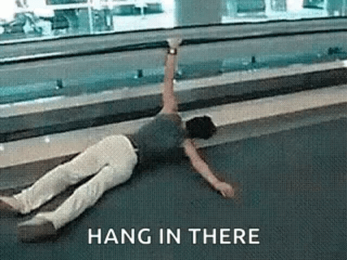 A Person Is Laying On The Floor With A Sign That Says Hang In There Above Them . GIF