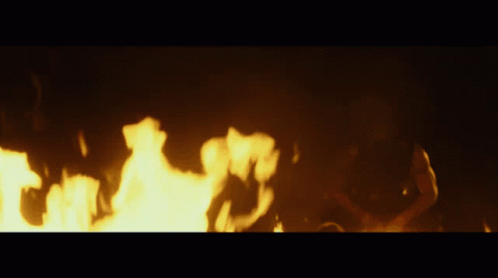 A Person Is Laying On The Ground In Front Of A Large Fire GIF