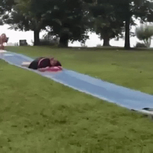 A Person Is Laying On Top Of A Blue Water Slide In A Park . GIF