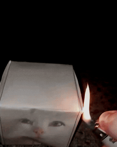 A Person Is Lighting A Lighter Next To A Box With A Picture Of A Face On It GIF