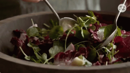 A Person Is Mixing A Salad In A Wooden Bowl With The Number 52 On The Bottom Right GIF