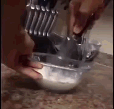 A Person Is Mixing Something In A Bowl With A Knife And Spoon . GIF