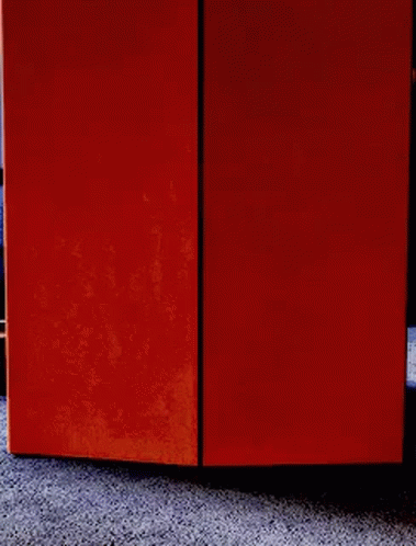 A Person Is Peeking Out From Behind An Orange Box On The Floor . GIF