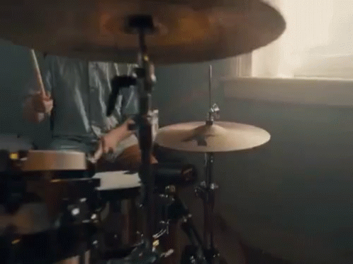 A Person Is Playing Drums In Front Of A Window In A Room . GIF