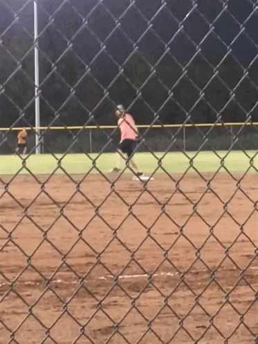 a person is playing softball on a field behind a chain link fence