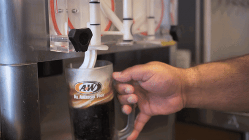 A Person Is Pouring A Beverage From A Machine That Says Aw GIF