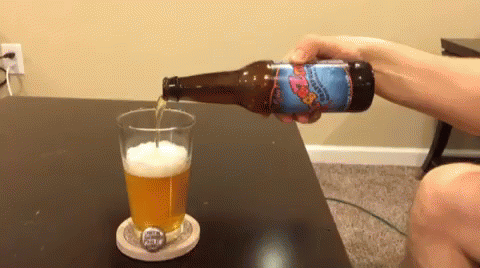 A Person Is Pouring A Bottle Of Beer Into A Glass On A Coaster GIF