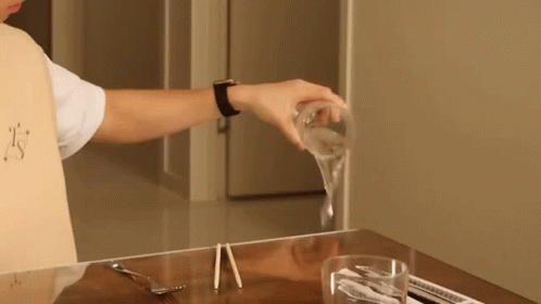 A Person Is Pouring A Glass Of Water On A Table With Chopsticks GIF