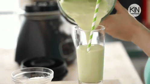 A Person Is Pouring A Green Smoothie Into A Glass With A Green Straw . GIF