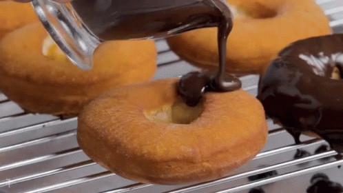 A Person Is Pouring Chocolate On A Donut On A Cooling Rack GIF