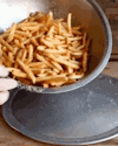 A Person Is Pouring French Fries From A Bowl Into A Pan . GIF