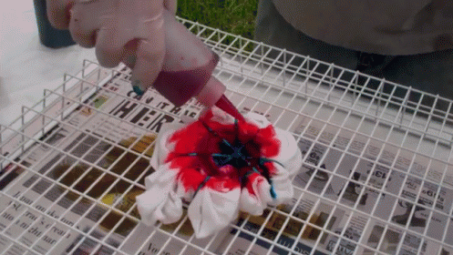 A Person Is Pouring Red And Blue Dye On A Piece Of Cloth With A Newspaper In The Background That Says ' Hier ' GIF