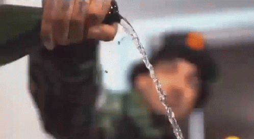 A Person Is Pouring Water From A Bottle Into Another Person 'S Face . GIF