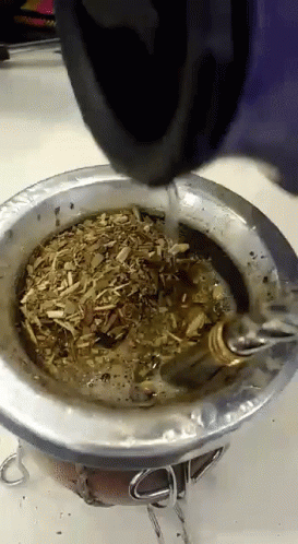 A Person Is Pouring Water Into A Metal Bowl With A Spoon In It GIF