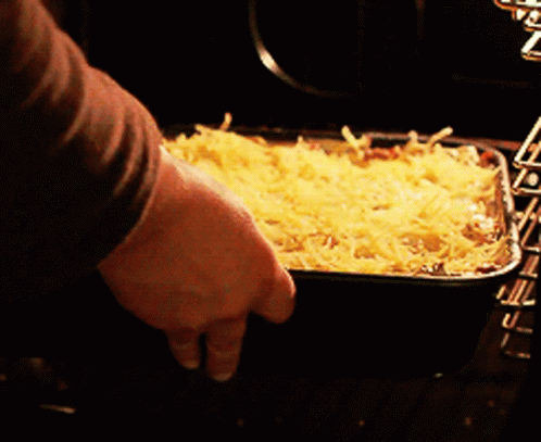 A Person Is Putting A Casserole Dish In The Oven GIF