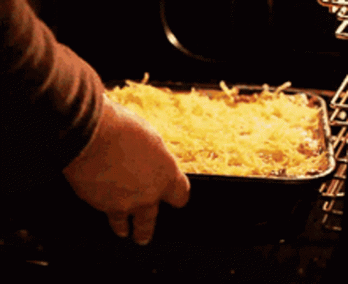 A Person Is Putting A Casserole Dish In The Oven GIF