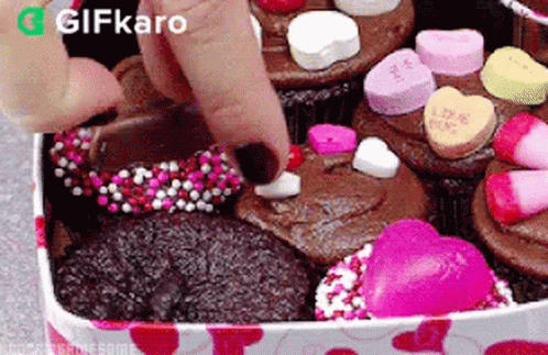 A Person Is Putting A Heart On A Cupcake In A Box Filled With Cupcakes . GIF