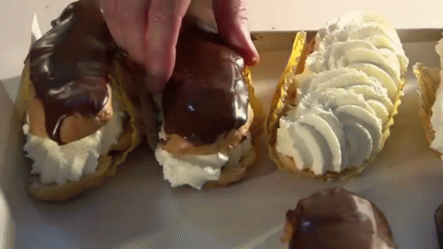 A Person Is Reaching For A Pastry With Whipped Cream GIF