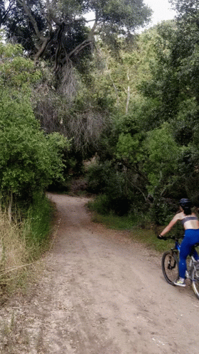 A Person Is Riding A Bike Down A Dirt Road GIF
