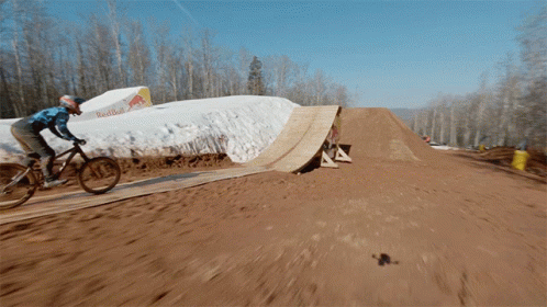 A Person Is Riding A Bike On A Dirt Track With A Red Bull Sign In The Background GIF