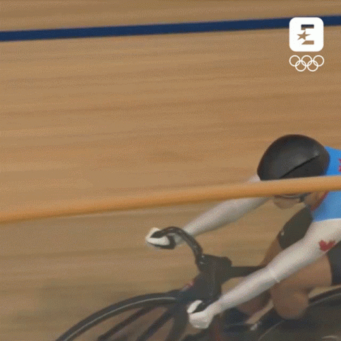 A Person Is Riding A Bike On A Track With The Olympics Logo In The Background . GIF