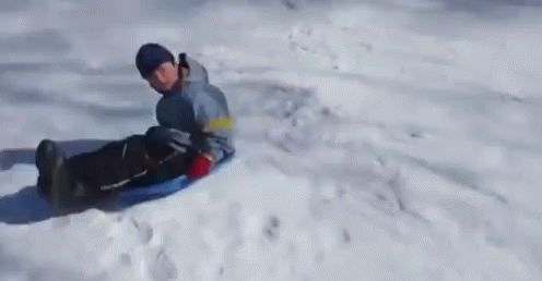 A Person Is Riding A Sled Down A Snow Covered Hill GIF