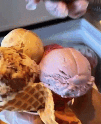 A Person Is Scooping Ice Cream Out Of A Waffle Cone In A Freezer . GIF