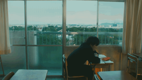 A Person Is Sitting At A Desk In Front Of A Window GIF