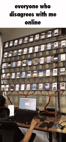 A Person Is Sitting At A Desk With A Laptop In Front Of A Wall Full Of Cell Phones GIF
