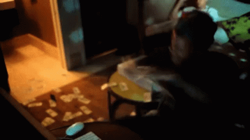 A Person Is Sitting At A Table With Cards On The Floor In A Dark Room GIF