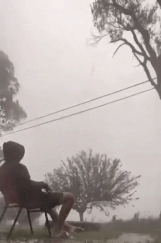 A Person Is Sitting In A Chair In The Rain With A Tree In The Background . GIF