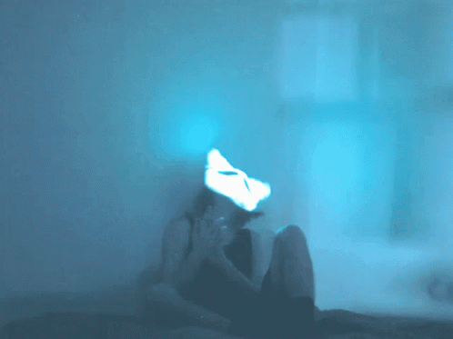 A Person Is Sitting In A Dark Room With A Cat Mask On Their Face GIF
