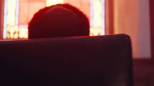 A Person Is Sitting In A Dark Room With A Red Light Behind Them GIF