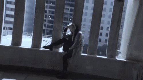 A Person Is Sitting On A Balcony Looking Out A Window At A City . GIF