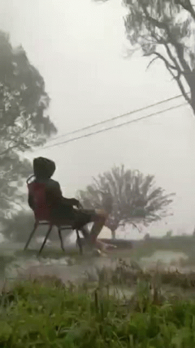 A Person Is Sitting On A Chair In The Grass In A Field . GIF