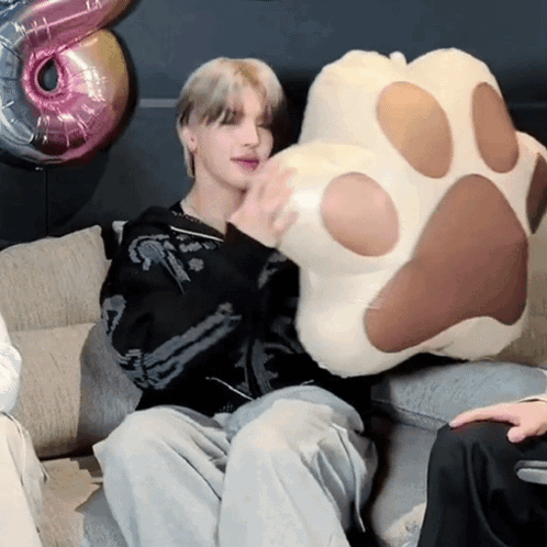 A Person Is Sitting On A Couch Holding A Paw Pillow GIF