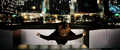 A Person Is Sitting On A Ledge Looking Out Over A City At Night GIF