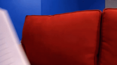 A Person Is Sitting On A Red Couch Holding A Piece Of Paper GIF