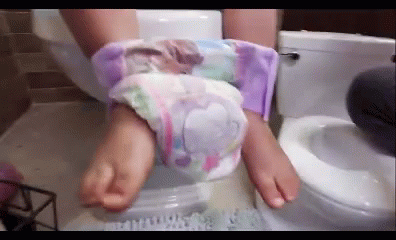 A Person Is Sitting On A Toilet With Their Feet In A Diaper . GIF
