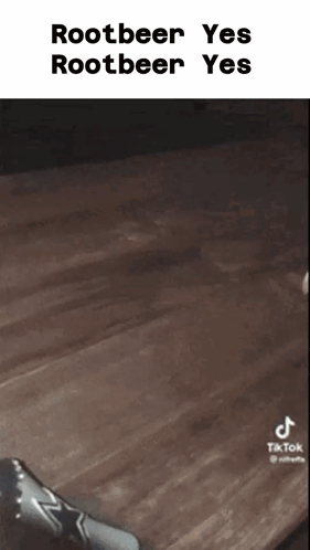 A Person Is Sitting On A Wooden Table With A Bottle Of Rootbeer In Front Of Them . GIF