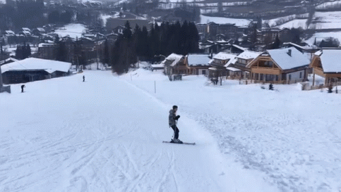 A Person Is Skiing Down A Snow Covered Slope With Houses In The Background GIF