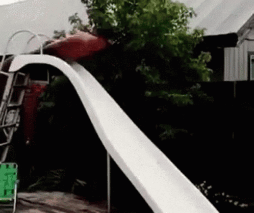 A Person Is Sliding Down A Slide In A Backyard GIF