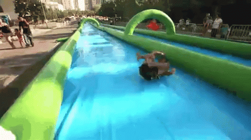 A Person Is Sliding Down An Inflatable Water Slide In A Park GIF